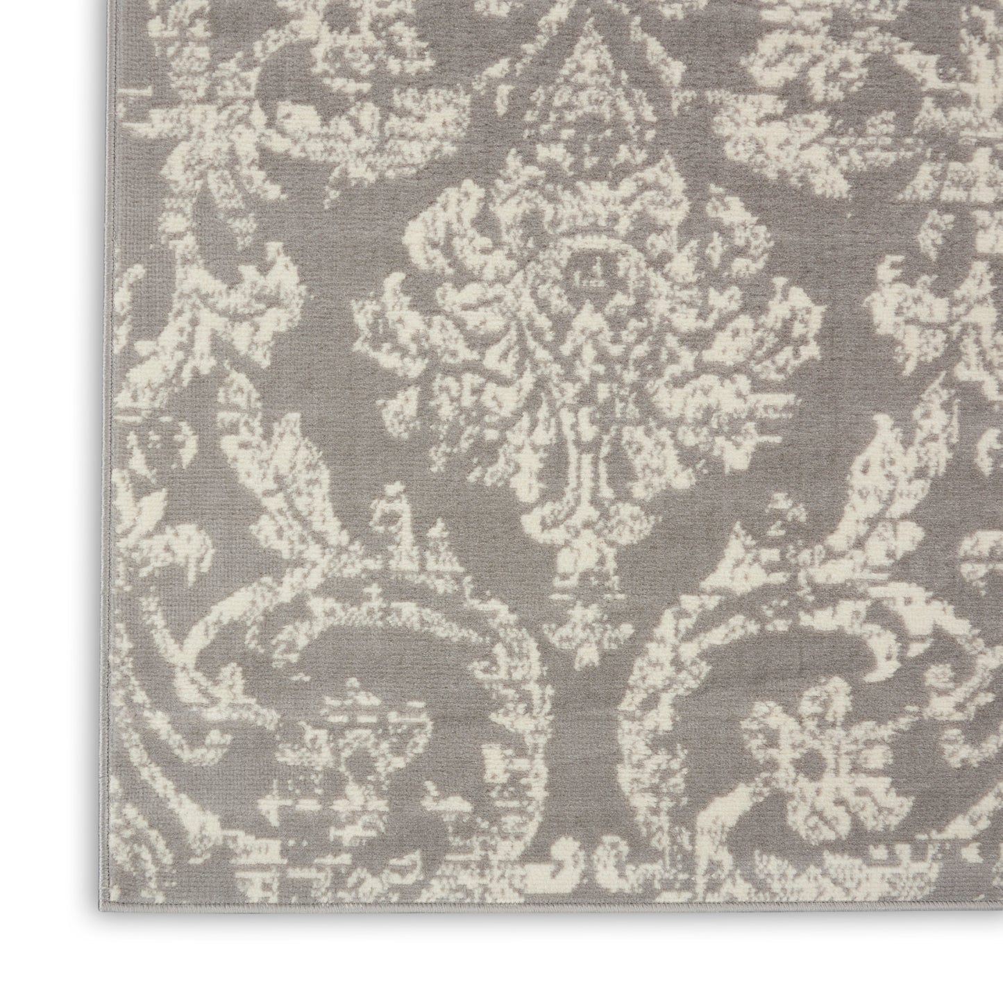 Close-up of gray damask rug with cream floral motif, textured woven surface, traditional elegant style.
