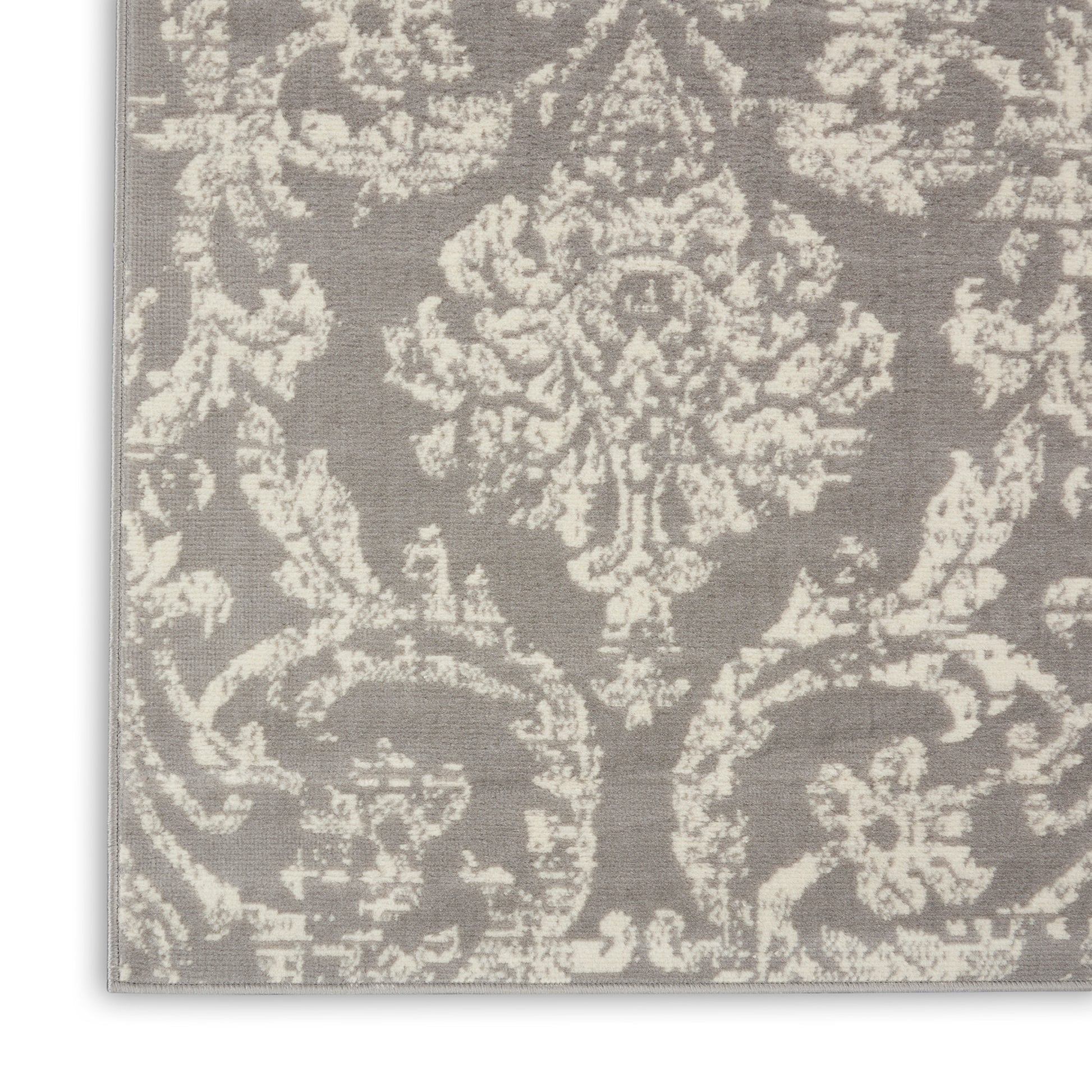 Close-up of gray damask rug with cream floral motif, textured woven surface, traditional elegant style.
