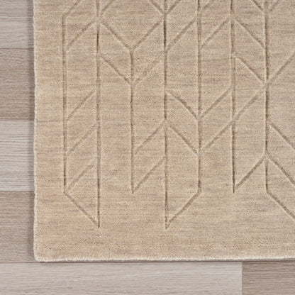 Beige textured rug with geometric chevron/leaf pattern and fringe along left edge on light wood floor.
