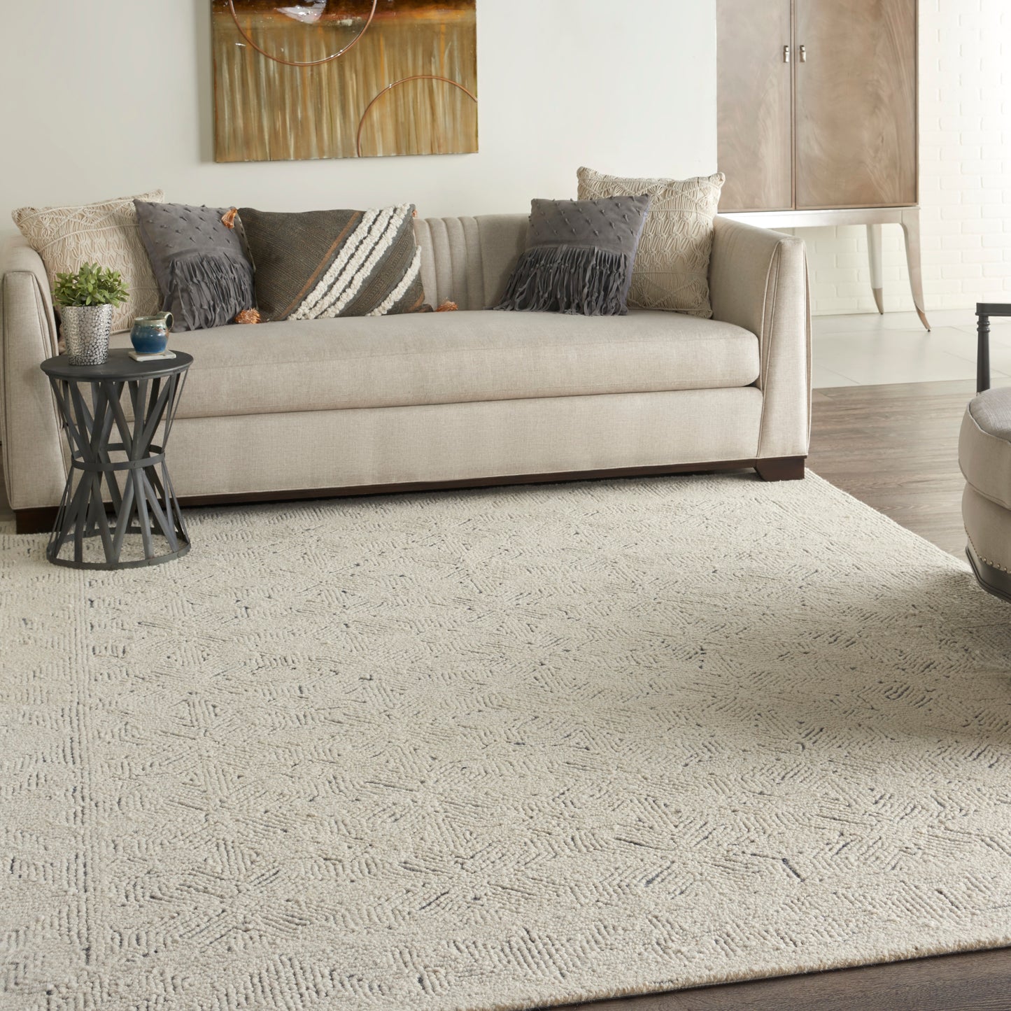 Beige fabric sofa, textured cream rug, neutral pillows, round metal side table, gold-accent wall art in a living room.