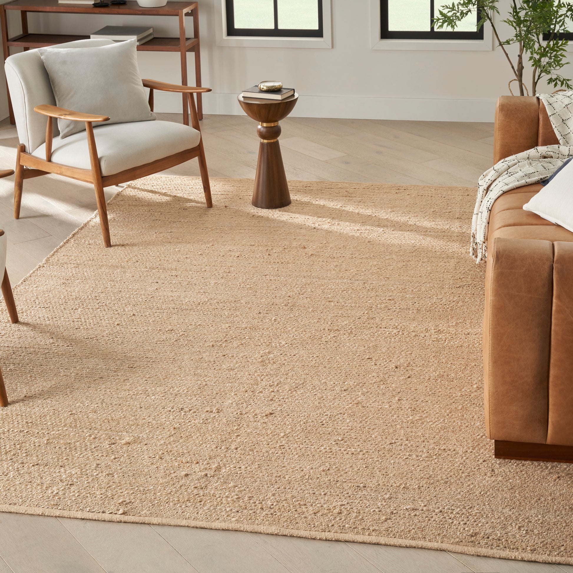 Natural beige jute rug anchors a cozy living room with tan leather sofa, light gray accent chair, & wooden side table.