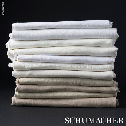 Stack of folded neutral linen textiles in cream, beige and white tones with varied textures on a dark background