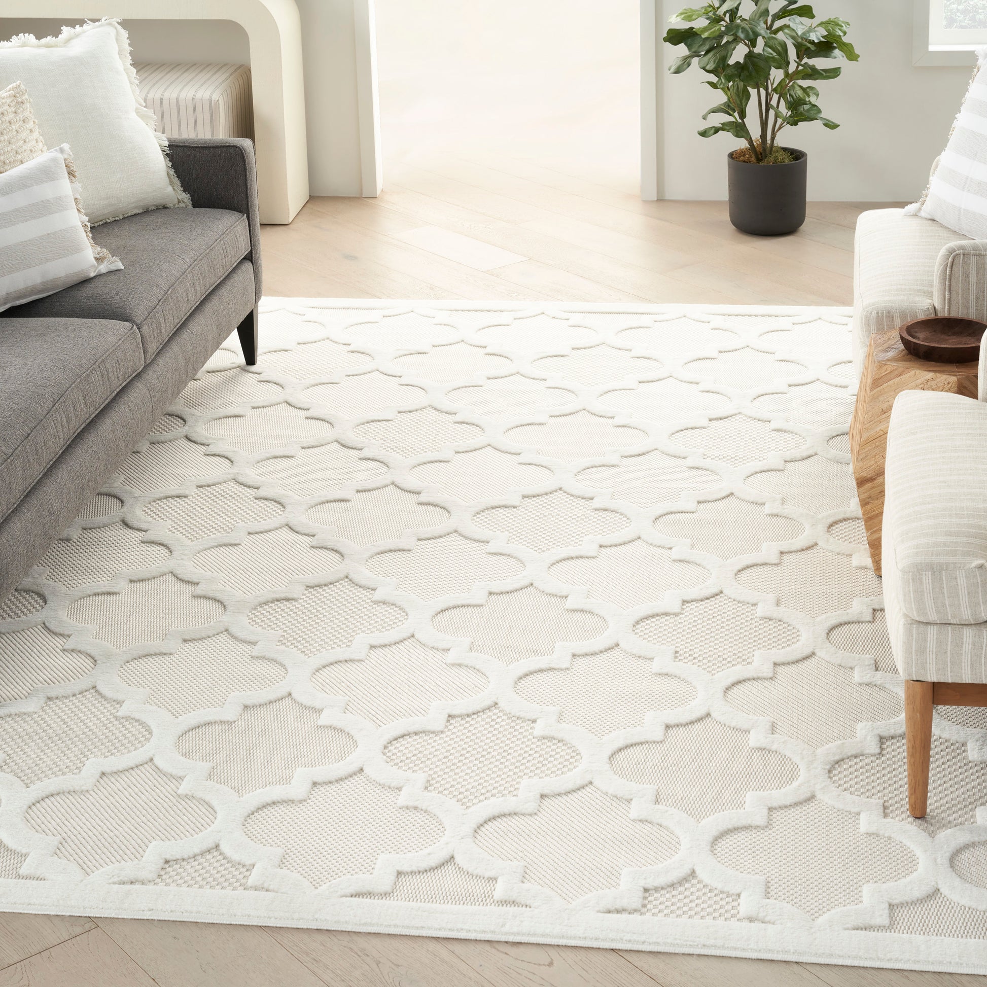 Cream textured area rug with interlocking quatrefoil lattice in white, in a contemporary living room with gray sofa and white armchair.