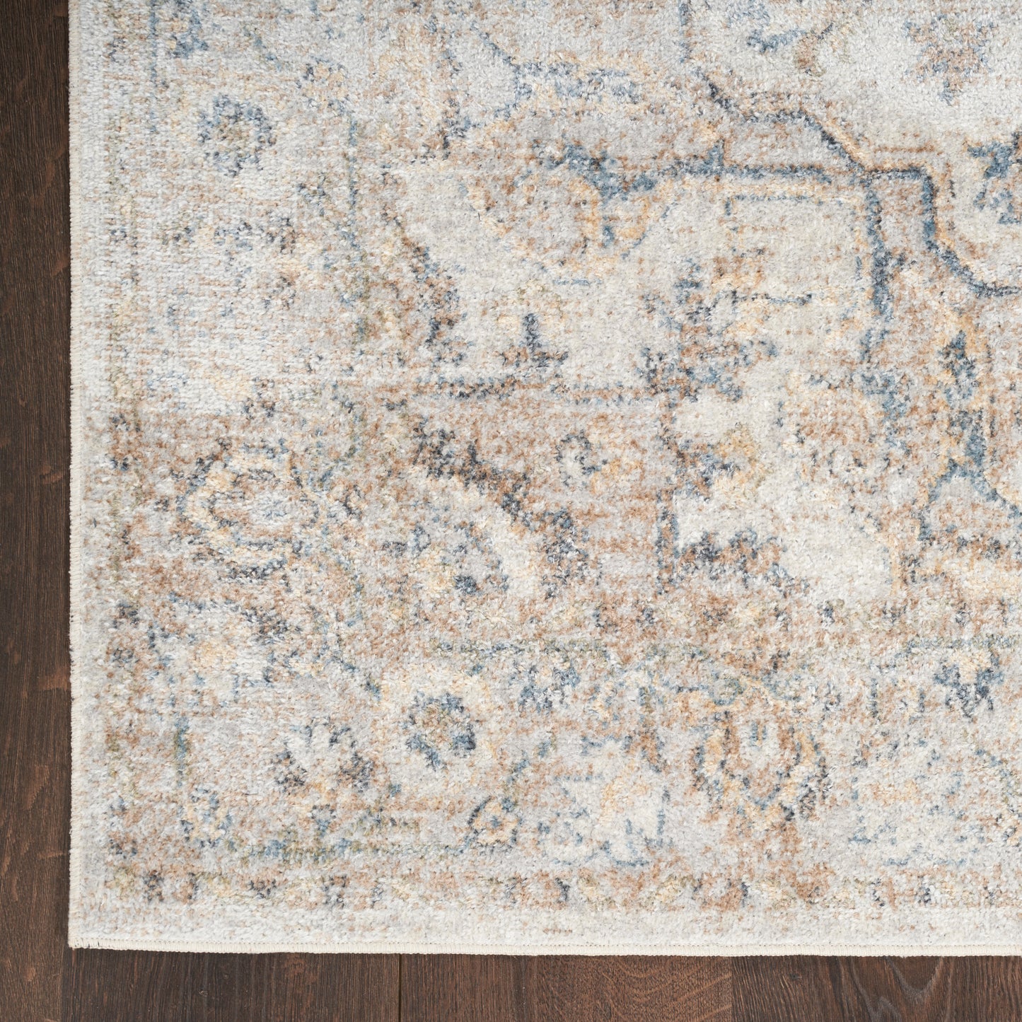 Cream, blue and beige distressed oriental rug with floral motifs and white fringe on dark wood floor.