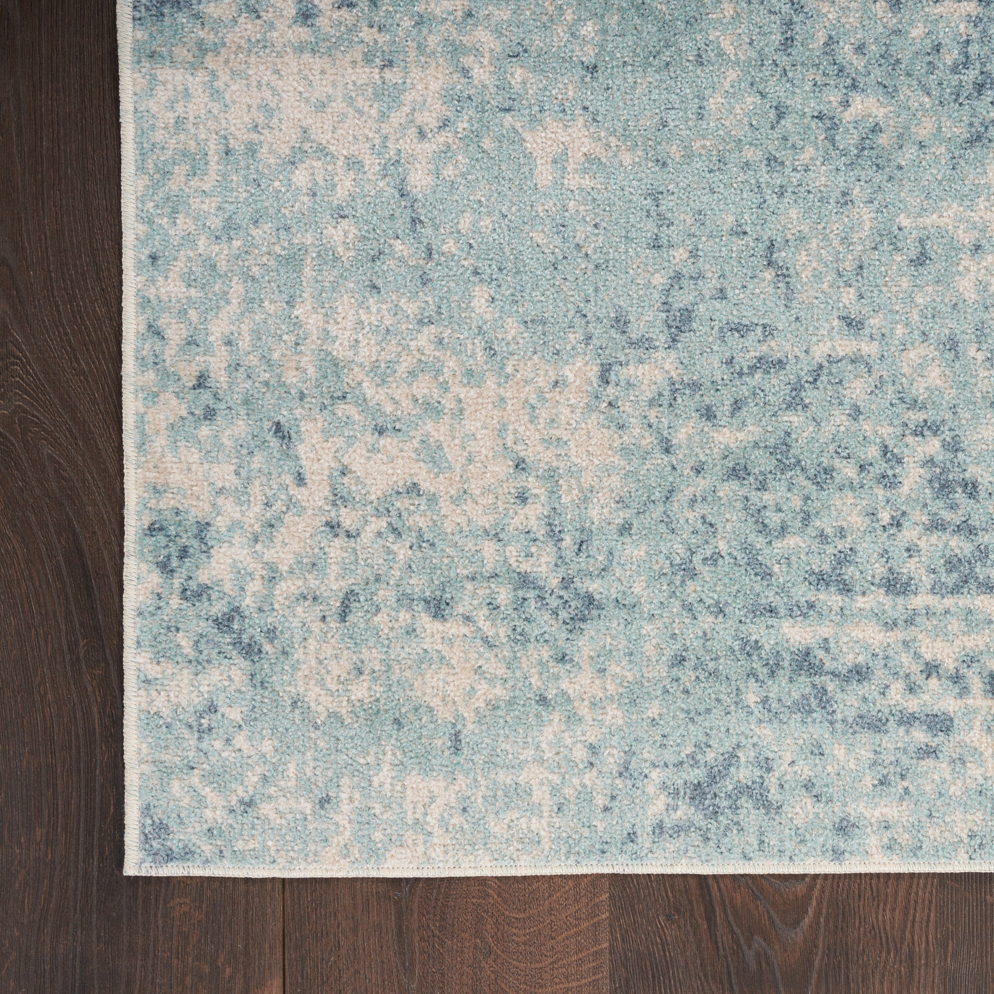 Blue and cream abstract-pattern rug with a faded design on dark wood floor; corner visible.