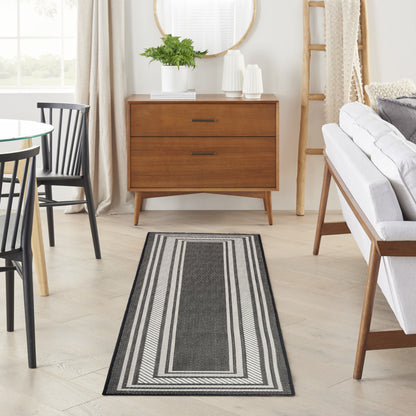 Long gray striped rug with black and white borders in a bright mid-century living room beside a wooden dresser and sofa.