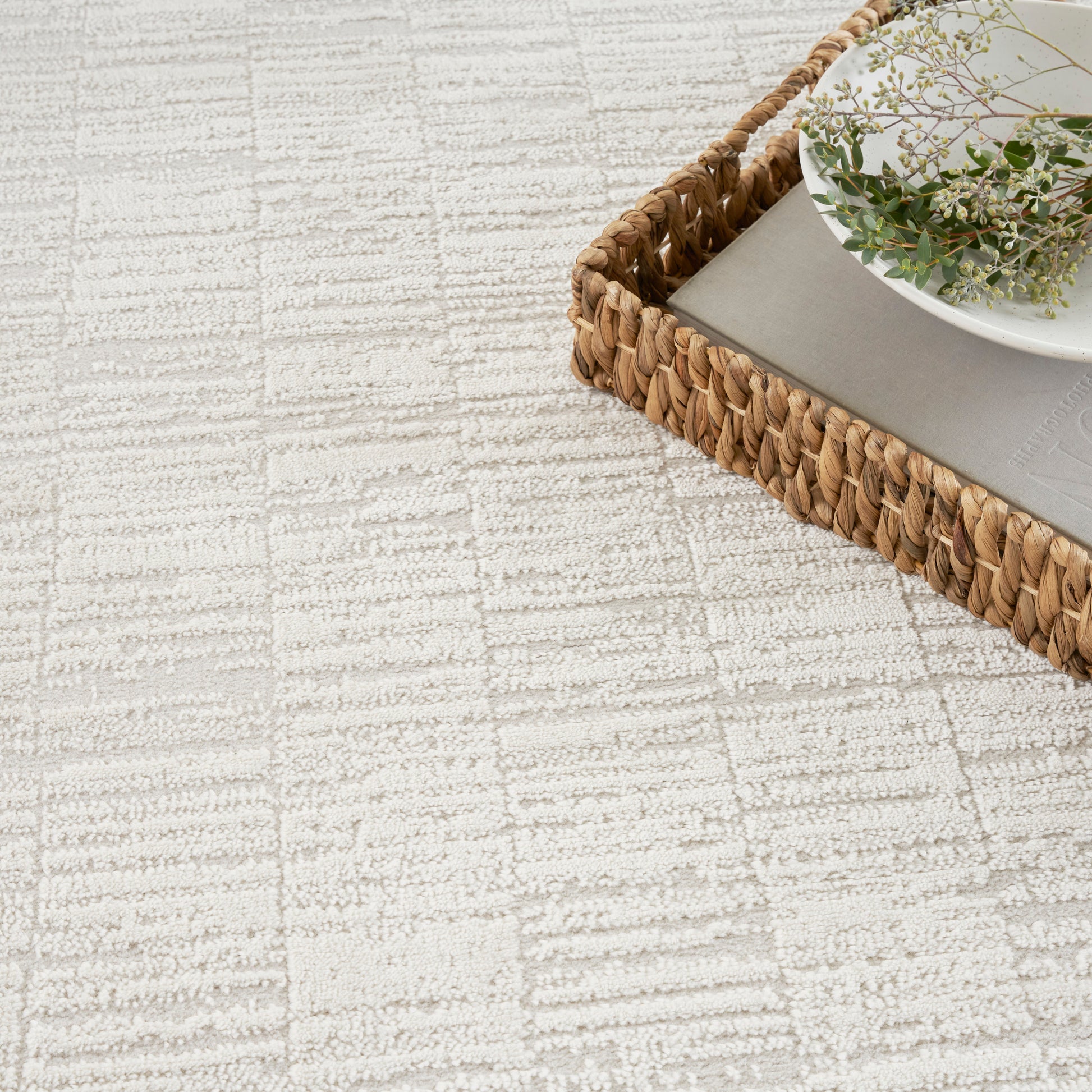 Natural woven rattan tray holding a white plate with greenery on a beige textured rug.