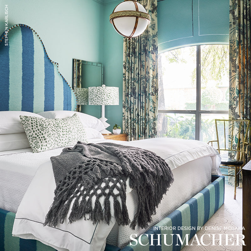 Bedroom scene featuring teal striped upholstery fabric on a bed, white linens, a gray fringed throw, botanical curtains & a round globe pendant light.