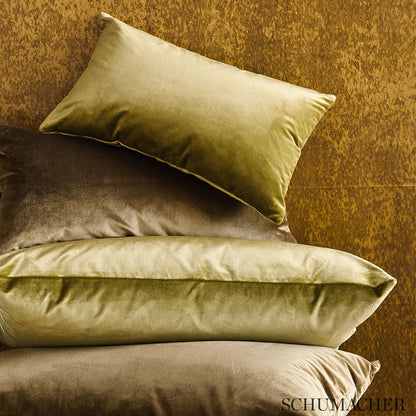Pile of olive, taupe and beige velvet cushions against a rust-toned backdrop.