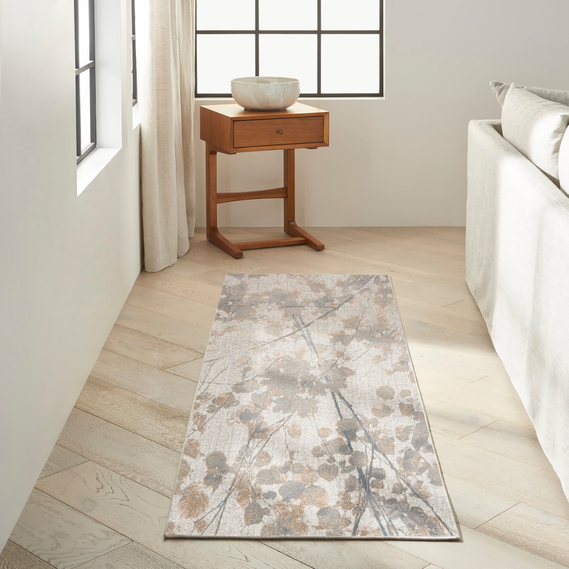 Neutral floral runner rug on light wood floor beside a small wooden side table with a white ceramic bowl.