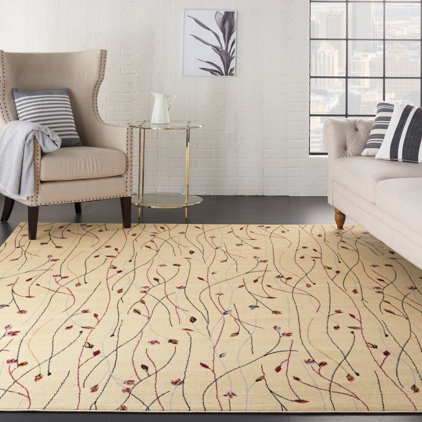 Cream rug with multicolored vines in a beige living room, complemented by a tufted armchair, light sofa and a gold-framed glass side table.