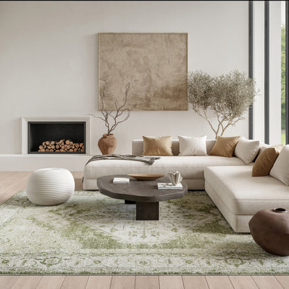 Neutral modern living room with beige sectional, round dark coffee table, white pouf, green patterned rug, and olive trees.