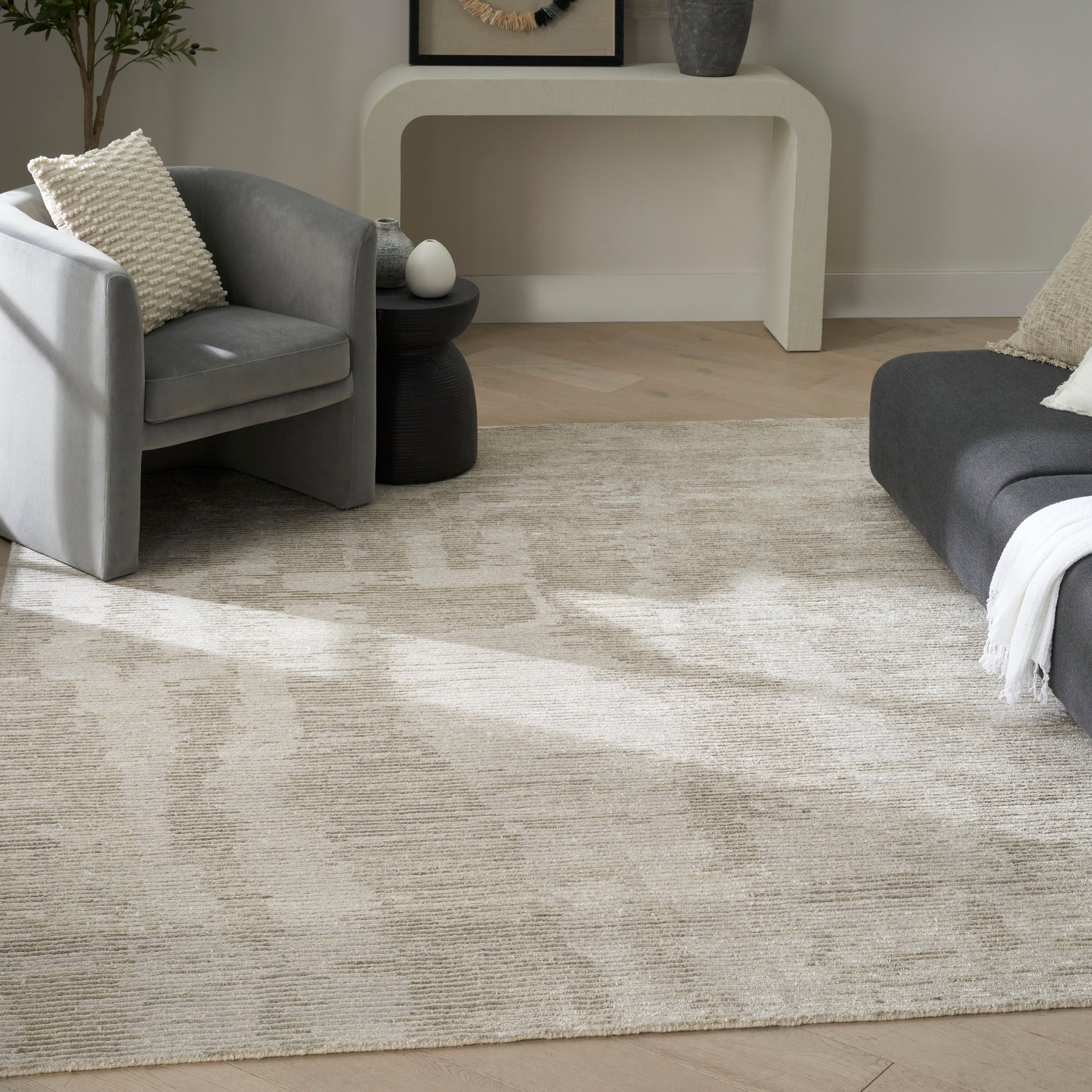 Neutral living room with beige abstract rug, gray sofa and armchair, cream curved console table.