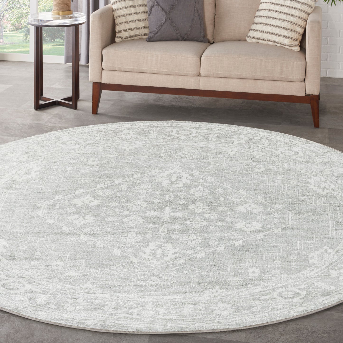 Round light-gray patterned rug in a living room with a beige sofa, decorative pillows, and a wooden side table.