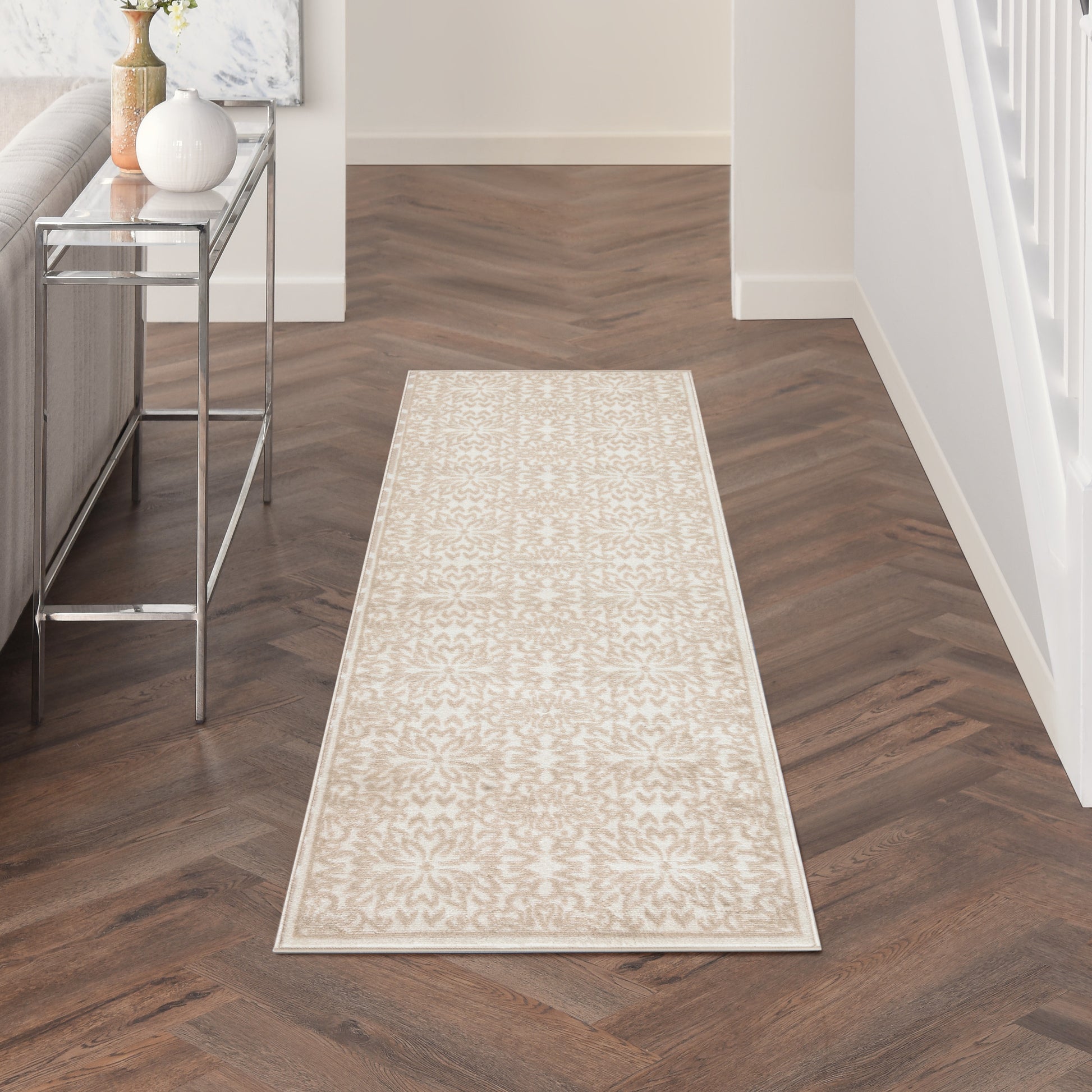 Long beige patterned runner rug with subtle floral motif on dark wood hallway floor, ivory border.