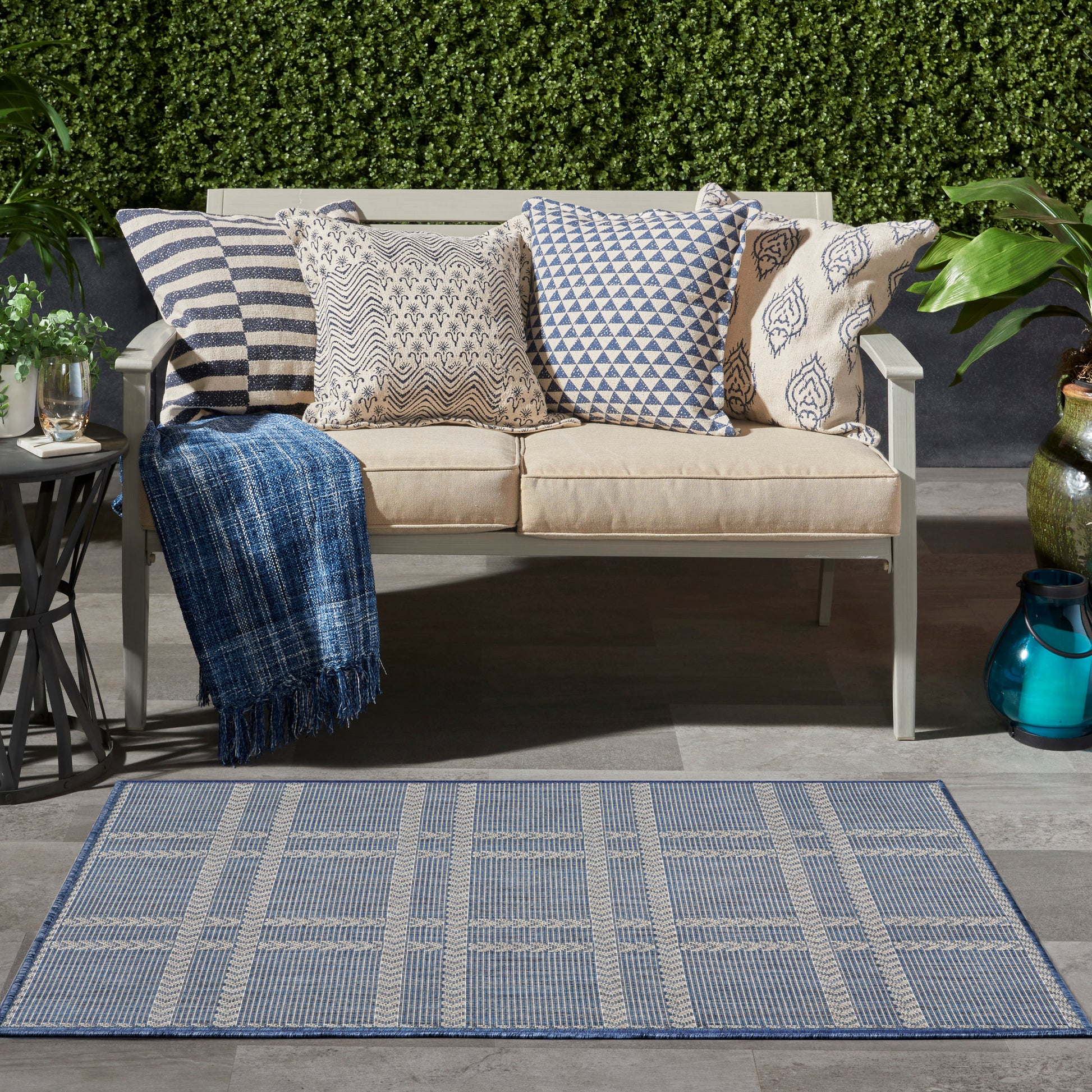 Blue plaid area rug in an outdoor setting amid greenery.