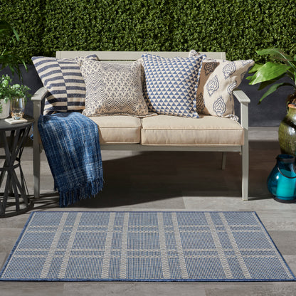Blue plaid area rug in an outdoor setting amid greenery.