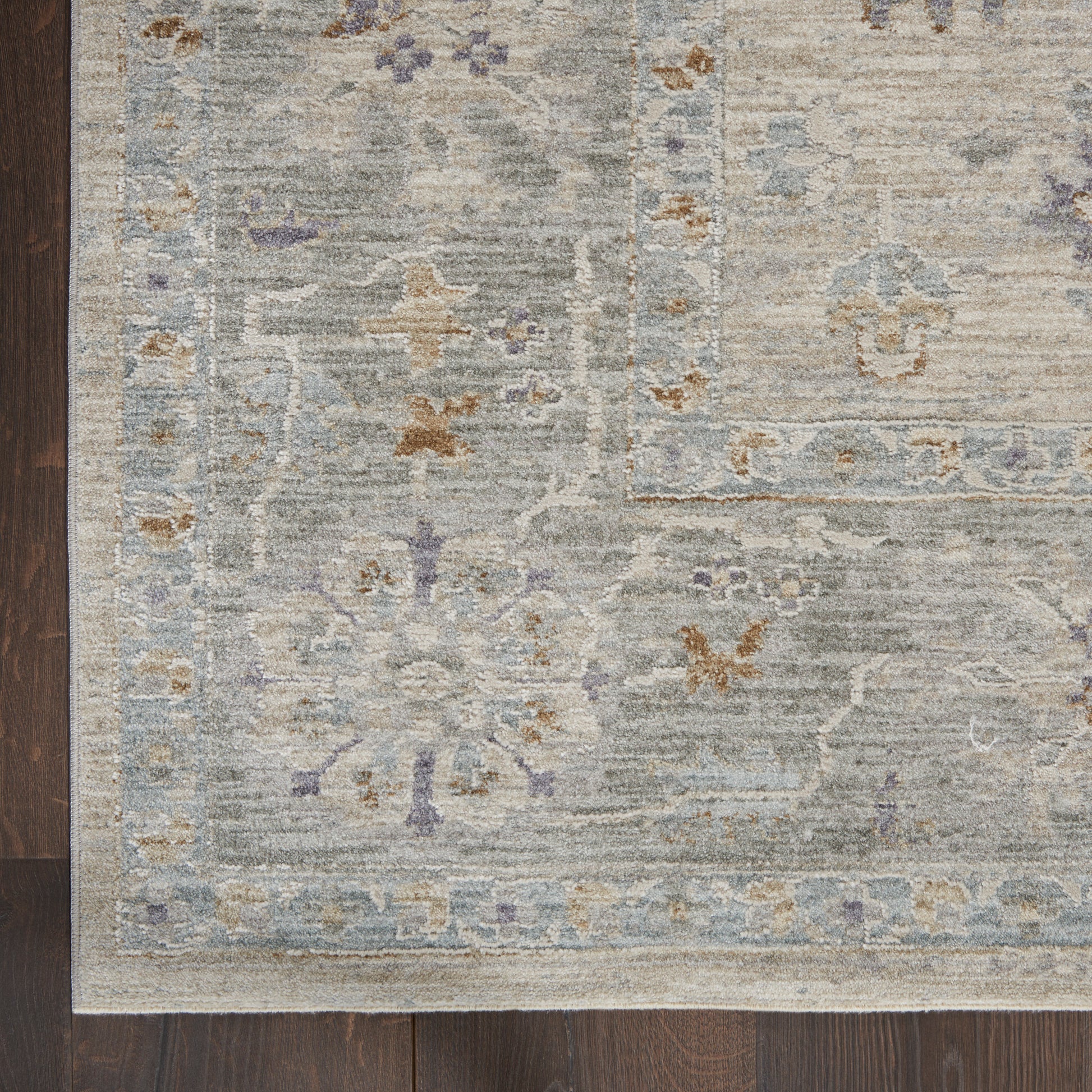 Muted gray-blue oriental rug with beige and pale blue floral motifs and a light border on dark wood floor.