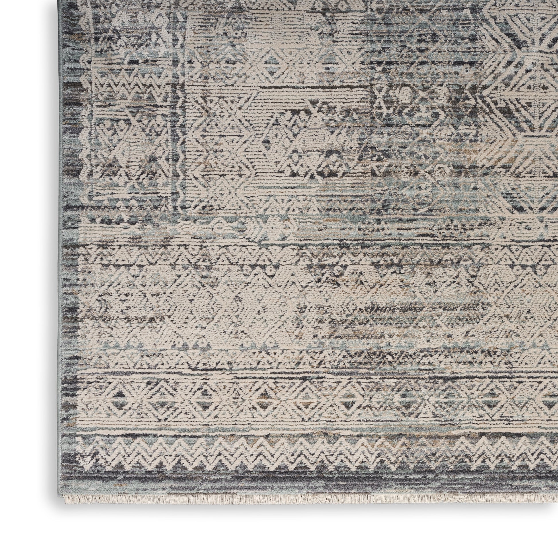 Rectangular boho-style area rug in muted blue-gray and cream with geometric diamond motifs and fringed border.