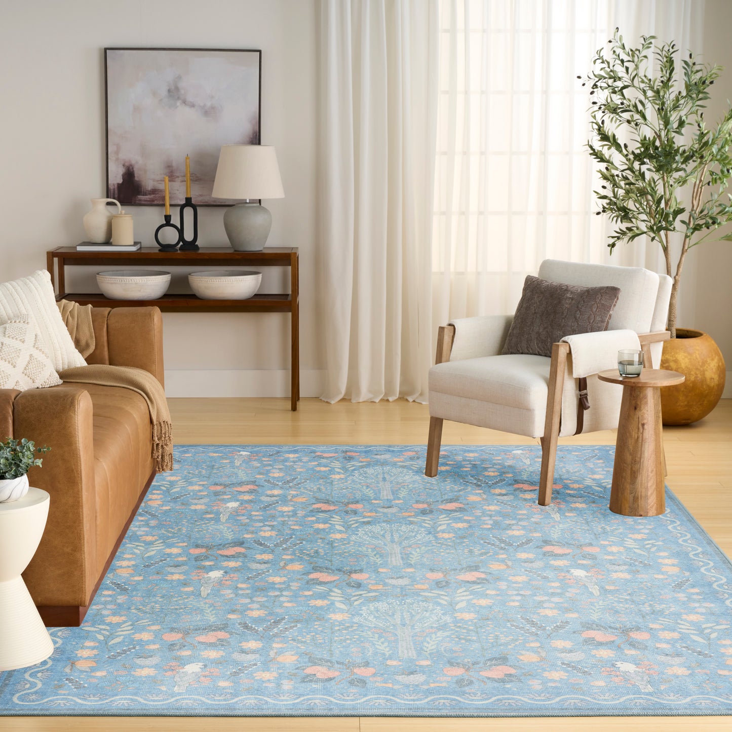 Cozy living room with blue patterned rug, brown leather sofa, cream armchair, wooden console, tall plant and sheer curtains.