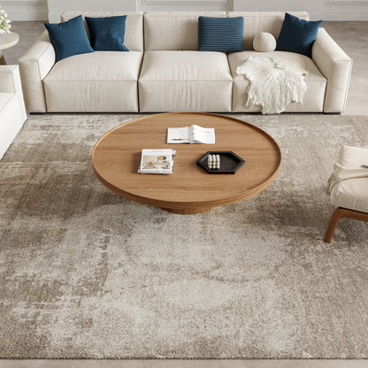 Round wooden coffee table on a light beige rug; cream sofa with blue pillows, white faux-fur throw, magazines.
