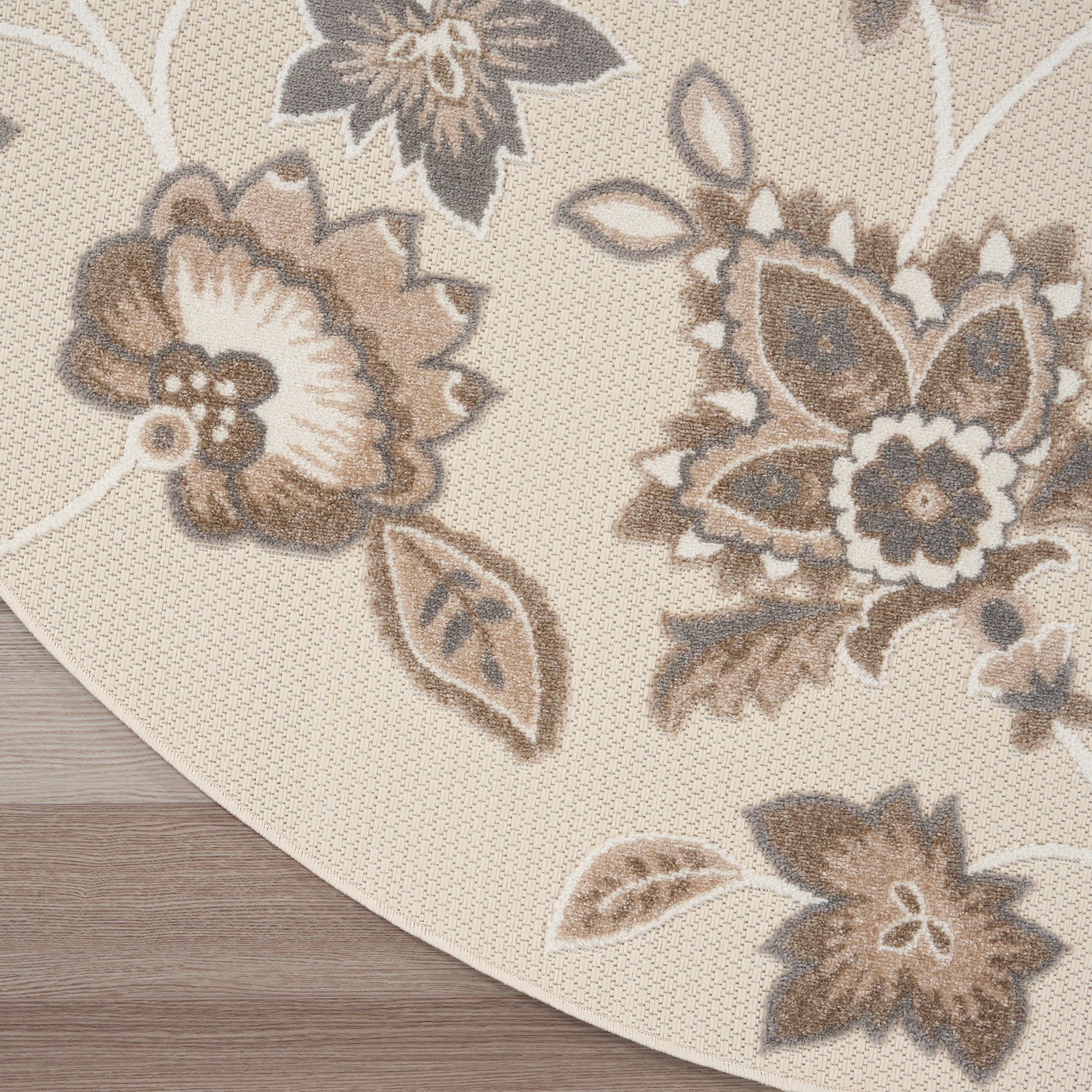 Round beige rug with cream and taupe floral pattern; woven textured surface and curved edge.