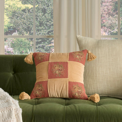 Emerald green tufted sofa with a patchwork orange-gold pillow and a beige lumbar cushion by a sunny window.