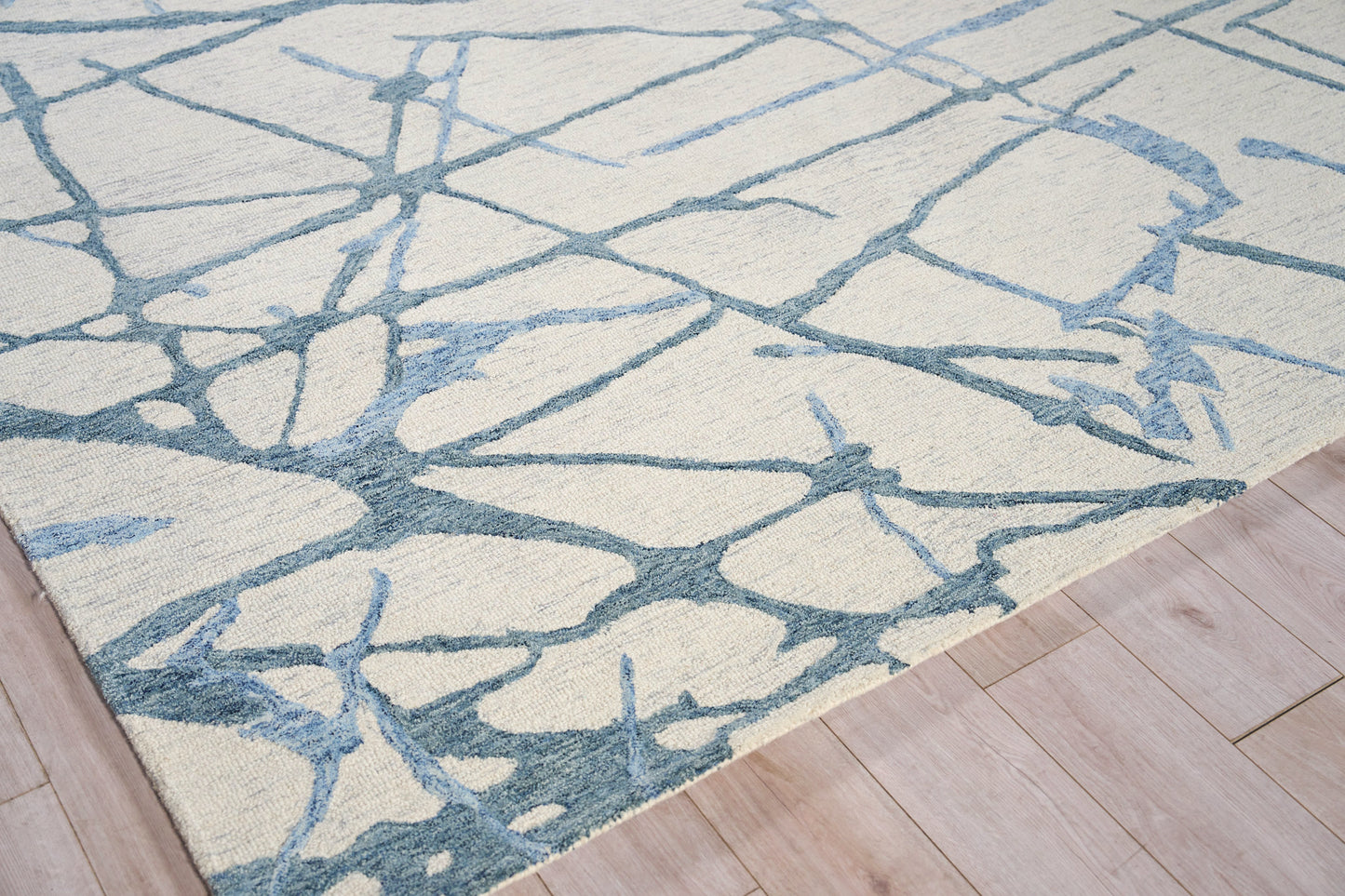 Cream area rug with blue-gray abstract branch pattern on light wood floor.