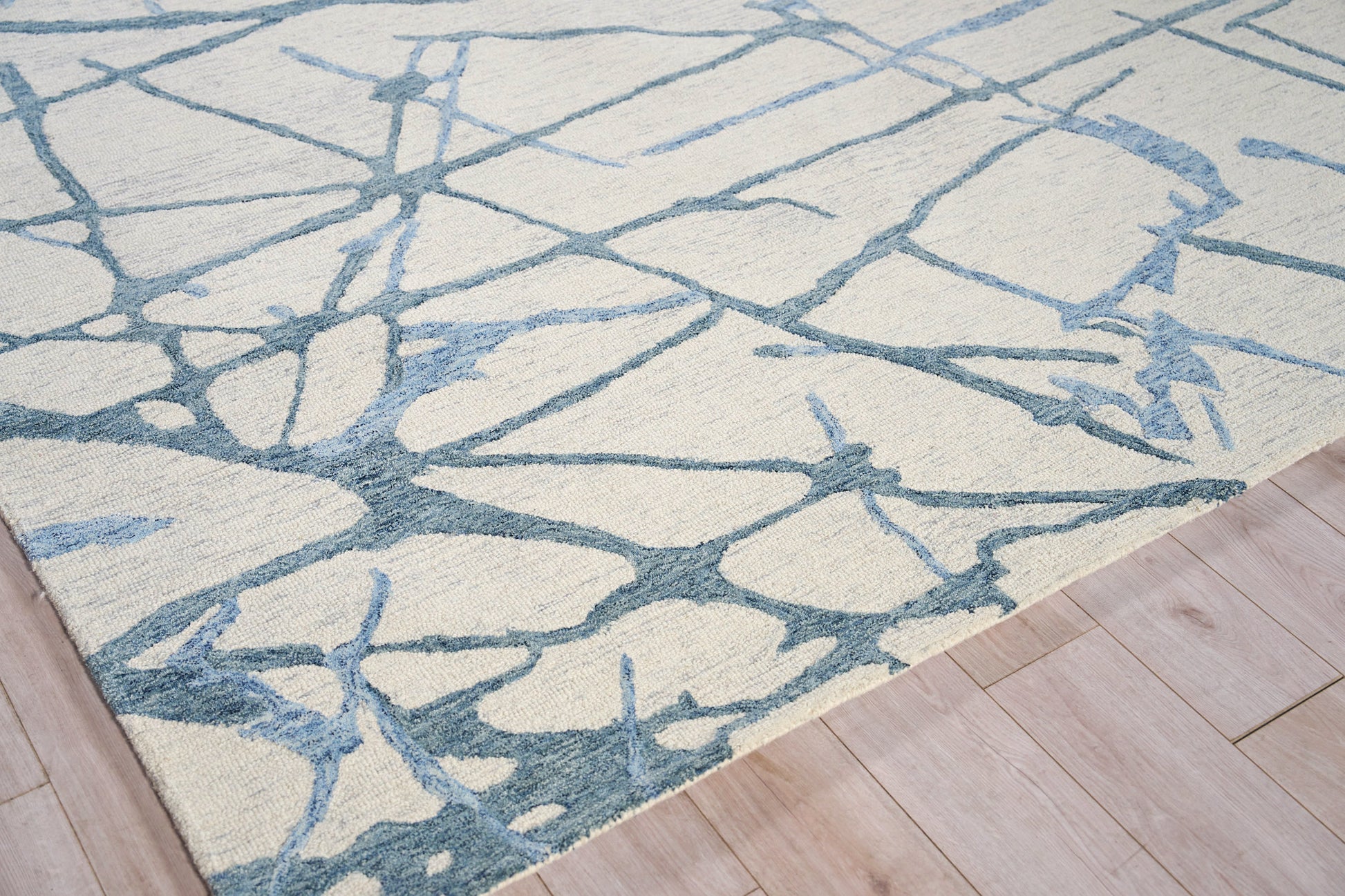 Cream area rug with blue-gray abstract branch pattern on light wood floor.