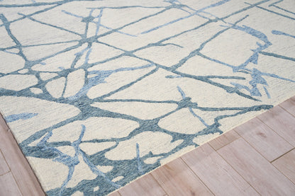 Cream area rug with blue-gray abstract branch pattern on light wood floor.