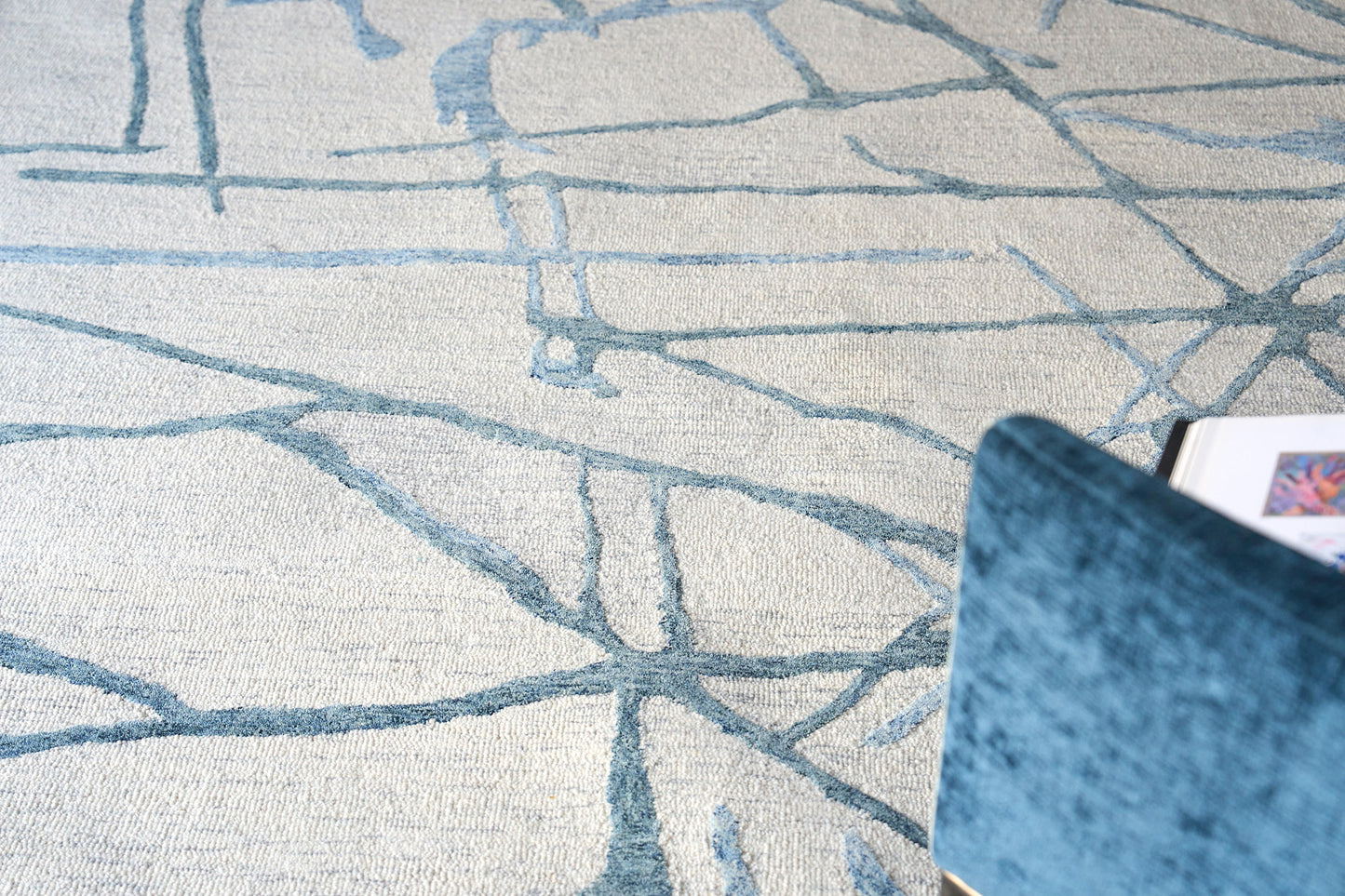 Blue velvet chair beside a beige hand-tufted rug with blue abstract lines, modern cozy living room scene.