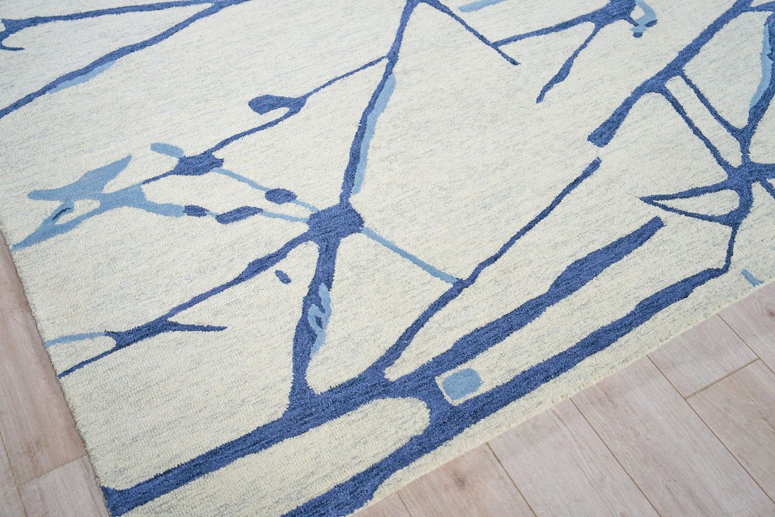 Beige rug with blue abstract branch pattern on light wood floor.