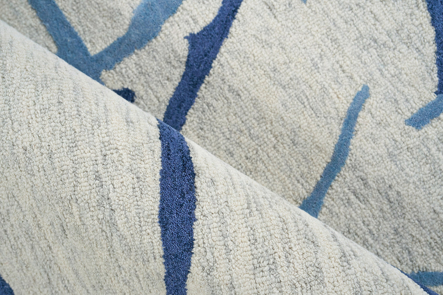 Beige textured rug with royal blue & light blue abstract lines; soft tufted pile, folded corner.