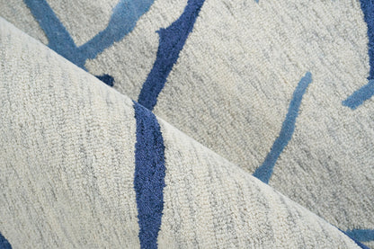Beige textured rug with royal blue & light blue abstract lines; soft tufted pile, folded corner.