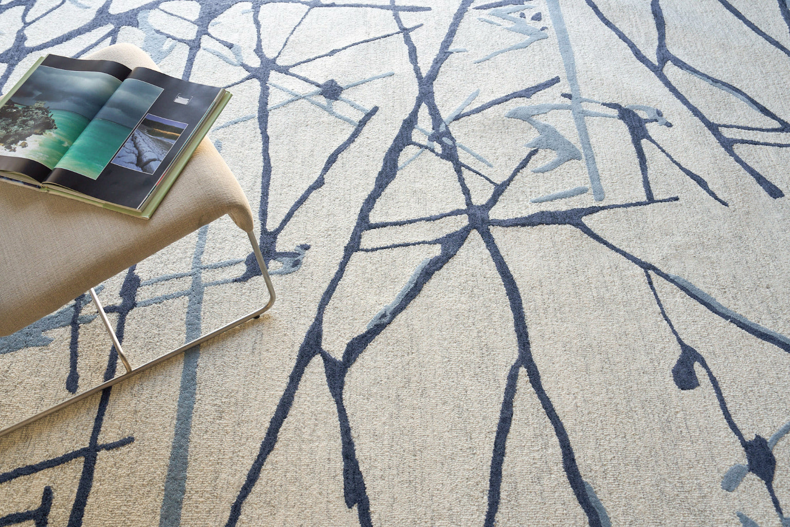 Beige textured rug with dark blue abstract branch pattern.