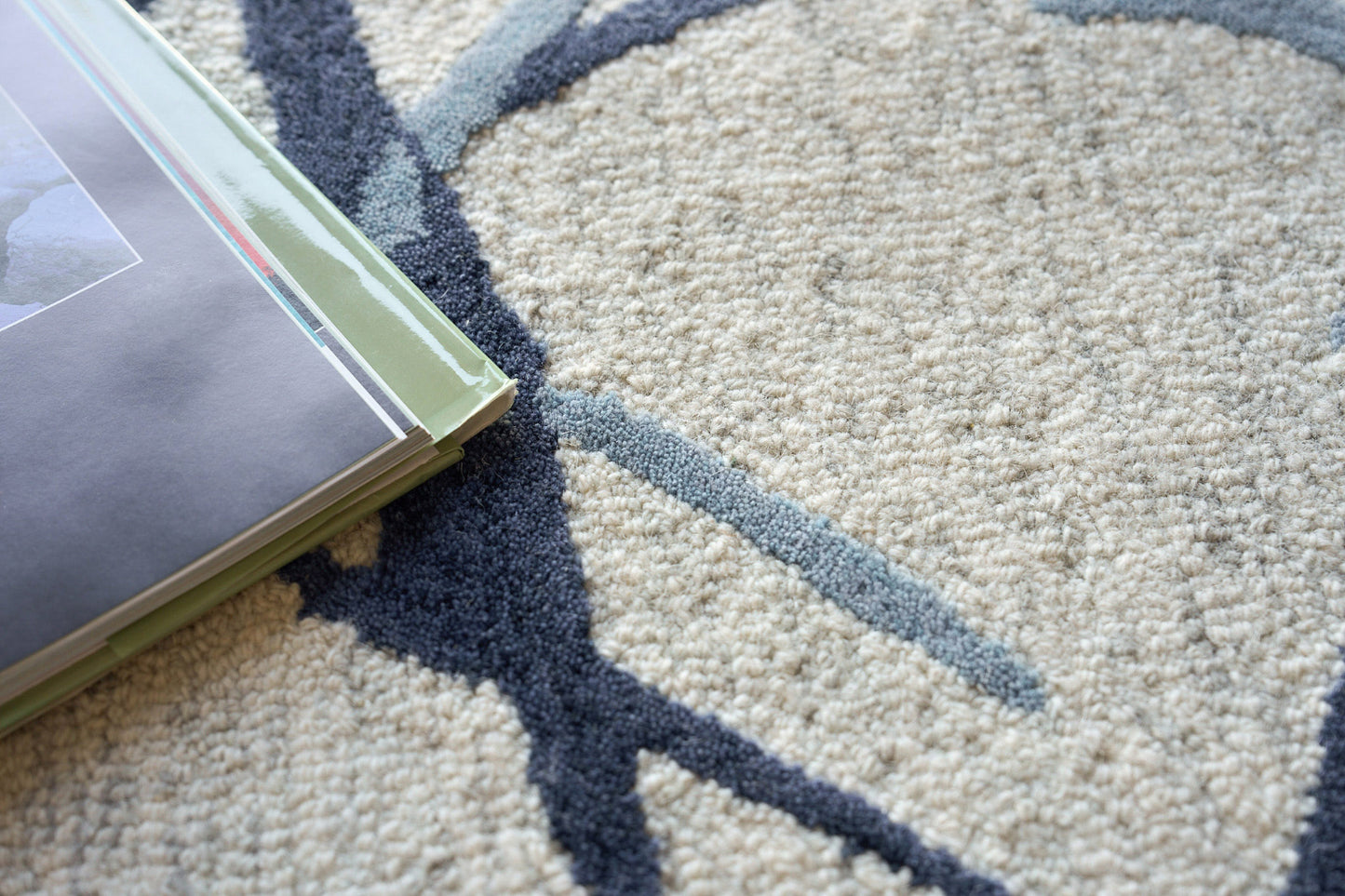 Cream and navy patterned rug with a stack of glossy magazines with green spines on top.