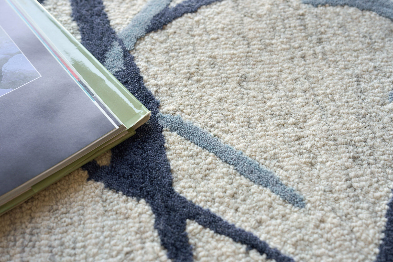 Cream and navy patterned rug with a stack of glossy magazines with green spines on top.