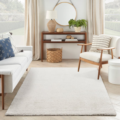 Cream textured area rug anchors a bright living room with mid-century wood chair, white sofa, round mirror, potted plant, and woven basket.
