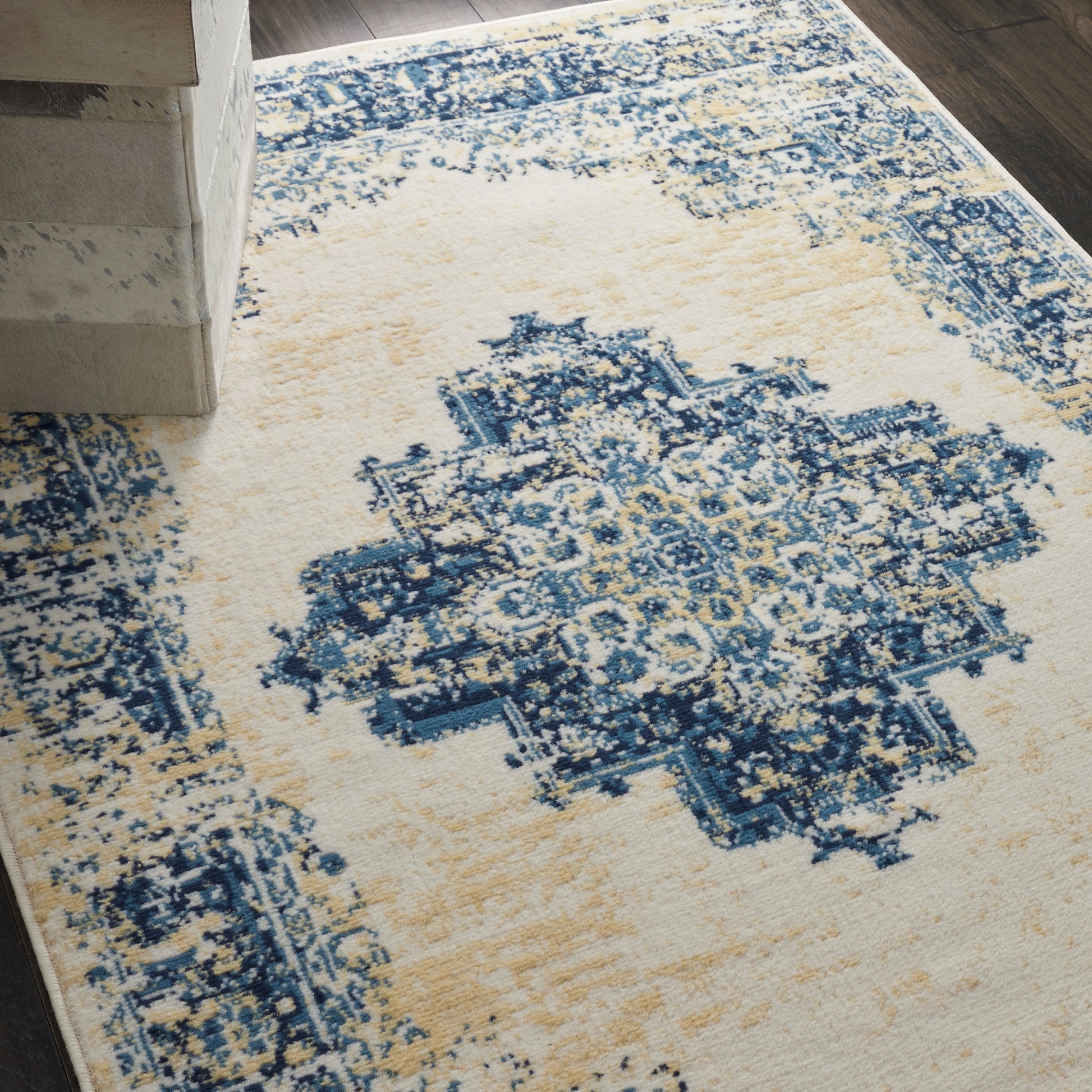 Rectangular cream and navy area rug with a blue ornate central medallion and distressed vintage pattern on dark wood floor.