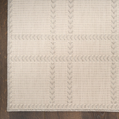 Beige woven area rug with subtle braided border and grid pattern, rectangular, on dark wood floor.