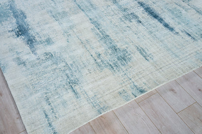Blue and cream abstract area rug with washed gradient pattern on light wood floor.