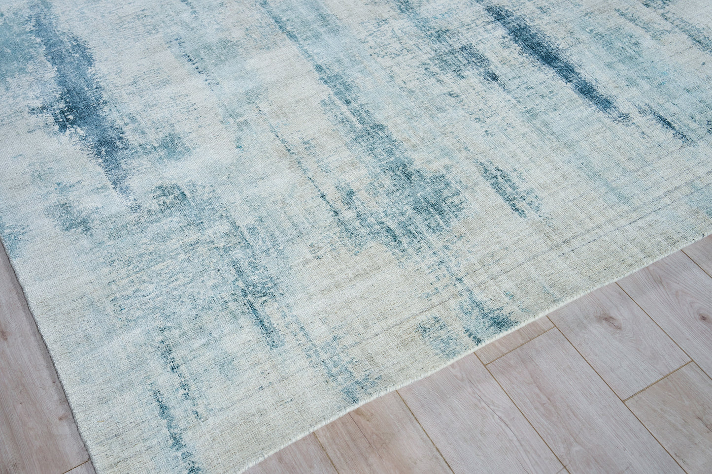 Blue abstract rug with teal and cream gradient on light wood floor.
