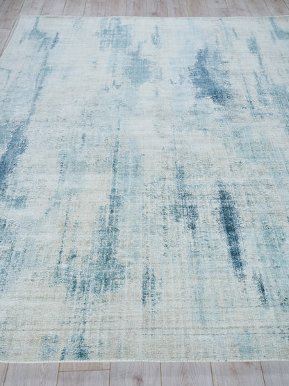 Rectangular rug with pale cream base and light blue distressed streaks on a light wooden floor.
