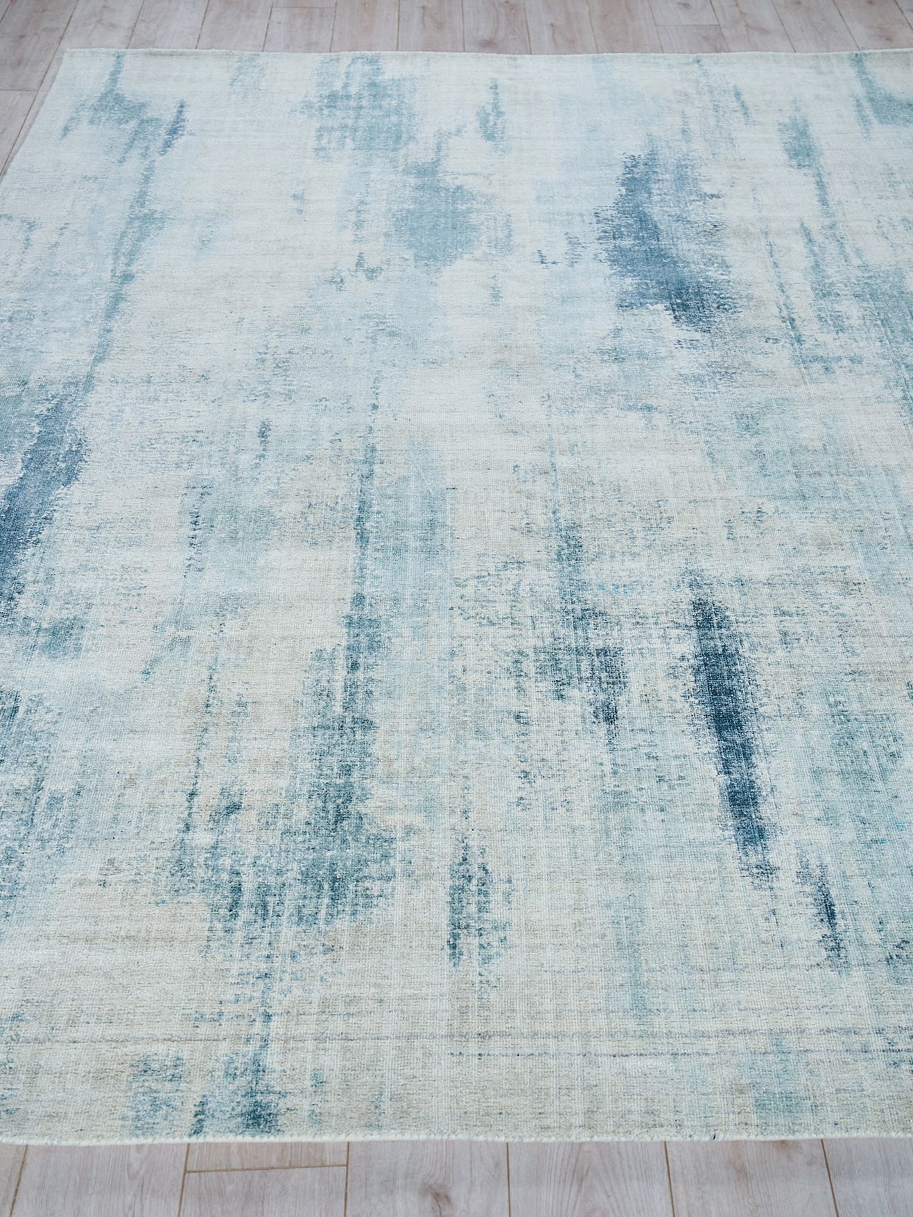 Blue & cream distressed abstract area rug with brush-stroke pattern on light wood floor.