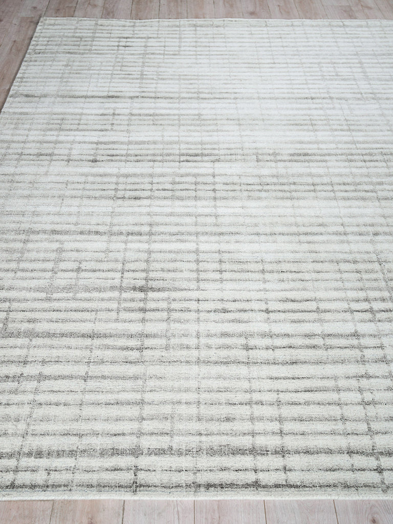 Light gray rectangular area rug with subtle darker grid lines; modern minimalist style on a wooden floor.