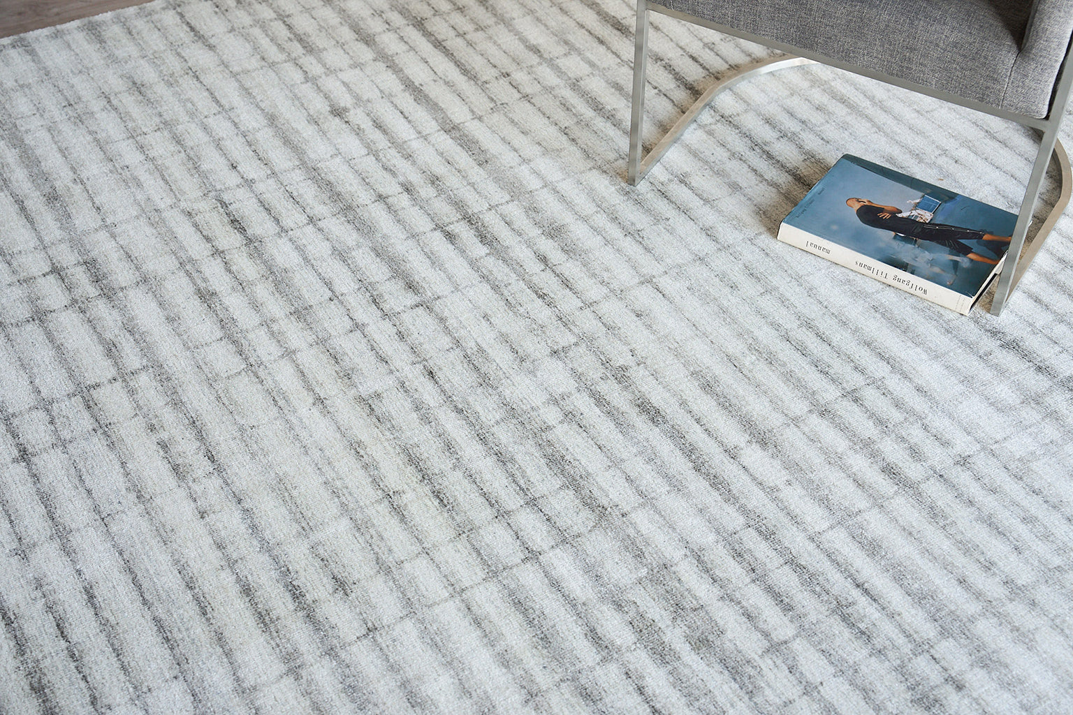 Light gray striped area rug with a soft woven texture; modern living room look with a gray chair nearby and a blue book.