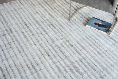 Light gray striped area rug with a soft woven texture; modern living room look with a gray chair nearby and a blue book.