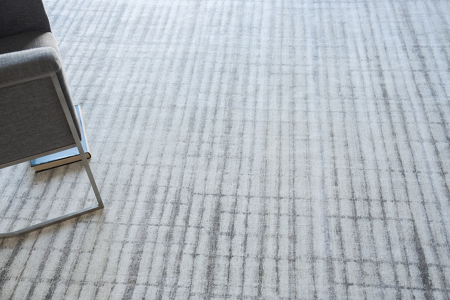 Gray striped rug under a metal-framed chair; a blue book peeks from beneath the chair leg.