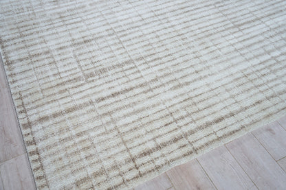 Rectangular cream-beige area rug with subtle tan distressed stripes, soft low-pile look, placed on light wood floor.