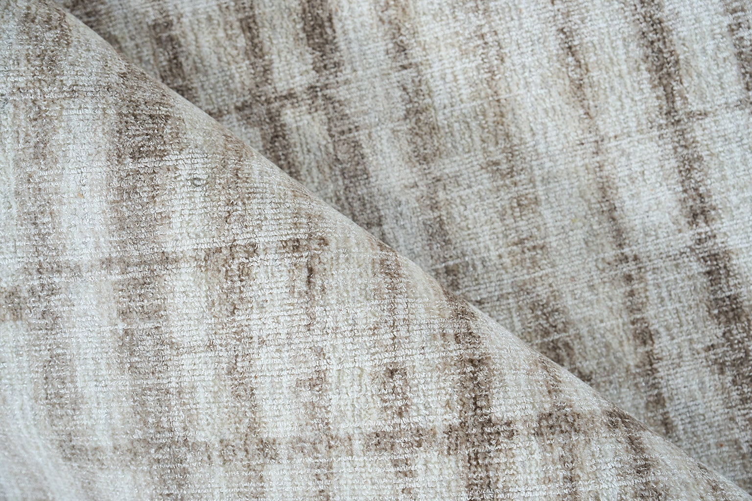 Neutral beige-taupe rug with subtle distressed pattern and soft woven pile, folded corner.